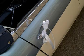 Classic car door handle adorned with a white ribbon bow for celebration.   Brussels, Belgium
