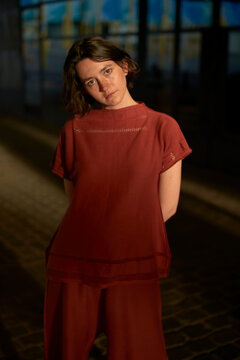 Woman in red outfit standing indoors, lit by warm light with a soft, thoughtful gaze. Brussels, Belgium
