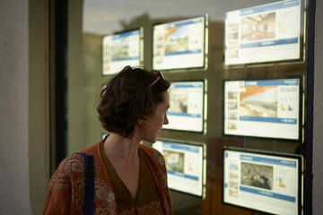 A woman looks at property listings displayed in a real estate agency window. Marseille, France