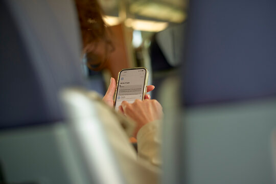 Person using a smartphone on a train with seats visible in a blurred background. Brussels, Belgium