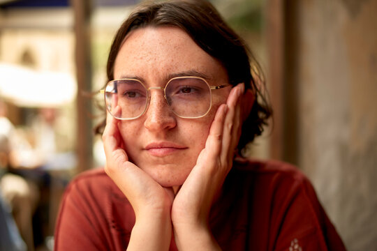 Young woman with short hair and glasses resting chin on hands in a thoughtful pose indoors. Marseille, France