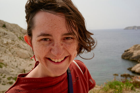 Smiling woman with short hair by rocky seaside under clear sky. Marseille, France