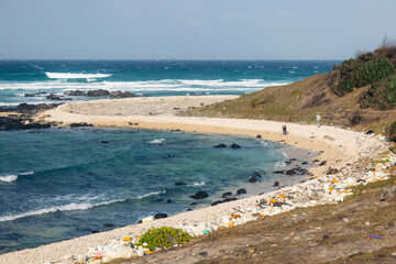 Secluded beach with gentle waves, rocky shore, and two people walking along the sand. Phu Quy island, BÏnh Thuan, Vietnam