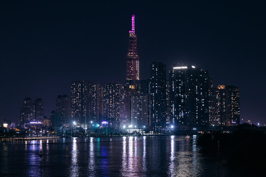 Illuminated skyscrapers reflecting in a calm river during a clear night in a cityscape. Ho Chi Minh City, Vietnam