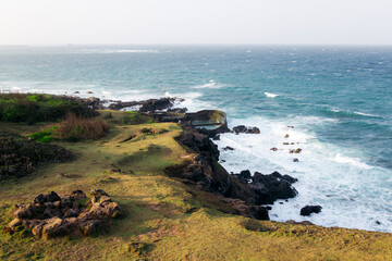 Coastal cliff with lush greenery overlooking a turbulent ocean and a distant horizon. Phu Quy island, BÏnh Thuan, Vietnam