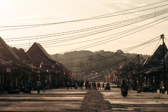 A bustling village street during sunset with silhouettes and distant mountains. Desa Hilisimaetano in South Nias, North Sumatra, Indonesia