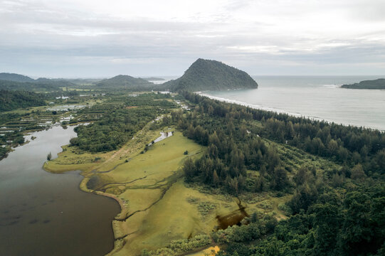 Aerial view of a lush, mountainous landscape meeting the ocean under a cloudy sky. Aceh Jaya Regency, Aceh, Sumatra, Indonesia