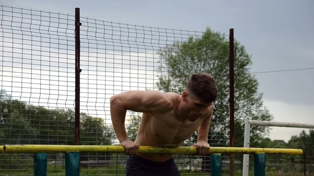Male shirtless athlete doing push ups on parallel bars at nature. Strong sporty man exercising at sports ground. Young sportsman training hard outdoor. Concept of active sportive lifestyle. Slow mo