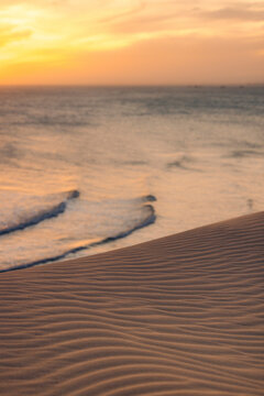 Golden sunset over rippled sand dunes leading to a calm ocean with gentle waves. Ke Ga, Binh Thuan, Indonesia