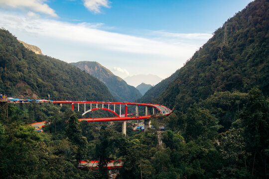 A vibrant red bridge snakes through lush green mountains under a clear blue sky.  Kelok 9, or the 9 hairpins, Harau, West Sumatra, Indonesia