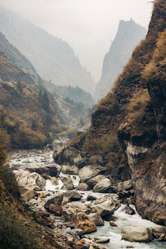 Majestic mountain landscape with a river flowing through rocky terrain under a misty sky. Road F36 of Annapurna in Gandaki Province, Nepal