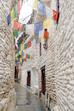 Narrow stone alleyway adorned with colorful prayer flags between rustic plastered buildings. Marpha, Annapurna, Mustang District of the Gandaki Province, Nepal