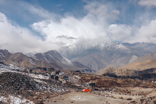 Village nestled in a mountain valley with snow-dusted peaks under a cloudy sky. Muktinath, Annapurna, Mustang District, Gandaki Province, Nepal