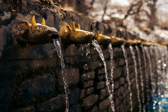 Stone wall with ornate faucet heads shaped as animals, water flowing steadily from each. Muktinath, Annapurna, Mustang District, Gandaki Province, Nepal