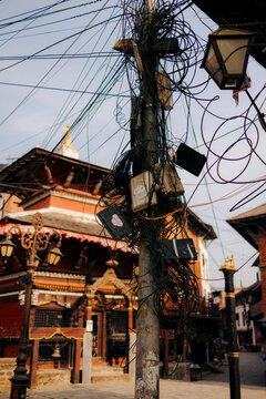 A tangled utility pole with cables in an urban area in front of a traditional building. Bandipur, Nepal