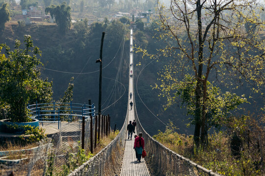 People walking on Kushma Suspension Bridge surrounded by lush greenery and distant hills. Kushma, Parbat district, Gandaki province, Nepal