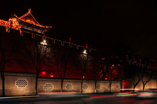 Historic building with illuminated red lights at night, trees casting shadows on the walls. Fortifications of Xi'an, China