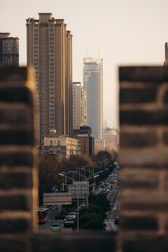 City skyline of tall buildings viewed through an ancient wall with a busy street below. Xi'an, China