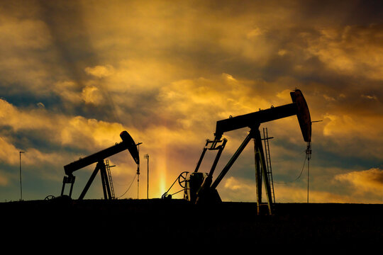 Silhouetted oil pumps against a dramatic, golden sunset sky. Alberta, Canada