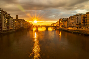 A breathtaking sunset over a river flanked by historic buildings, creating a golden reflection. Florence, Italy