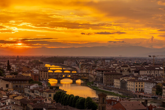 Aerial view of Florence at sunset with iconic bridges and Arno River under a vibrant sky. Florence, Italy