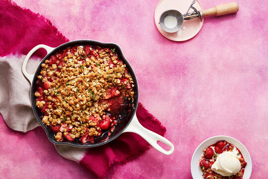 Strawberry crumble with ice cream on a pink background and a scoop nearby.