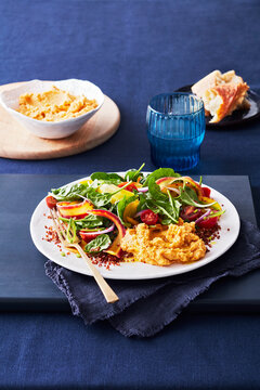 Fresh hummus with salad on a white plate, served with bread and blue glass.