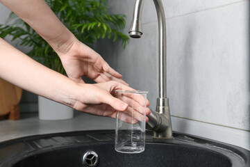 Woman taking sample of water from faucet indoors, closeup. Quality testing