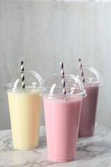 Milkshakes of different flavors in plastic cups on white marble table, closeup