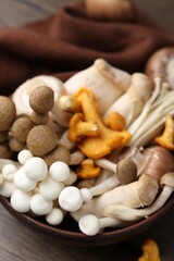 Different raw mushrooms in bowl on wooden table, closeup