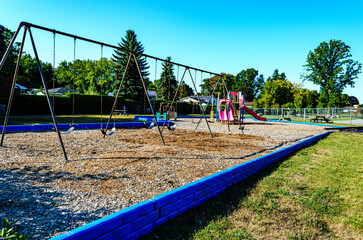 Empty school playground with swings and slides under a clear blue sky.