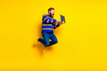 Young bearded man jumping with a laptop against a vibrant yellow background showcasing energy and dynamic expressions