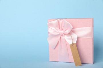 Gift box with blank tag on light blue background. Space for text