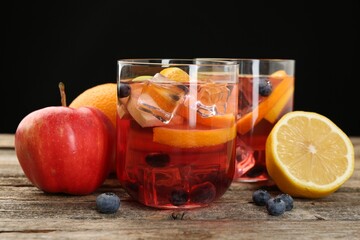 Tasty punch in glasses and fresh fruits on wooden table against black background, closeup. Refreshing drink