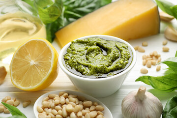 Fresh pesto sauce in bowl and ingredients on white wooden table, closeup