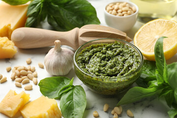 Fresh pesto sauce in bowl, ingredients and squeezer on white marble table, closeup