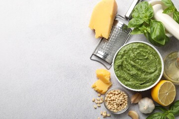 Fresh pesto sauce in bowl and ingredients on light grey table, flat lay. Space for text
