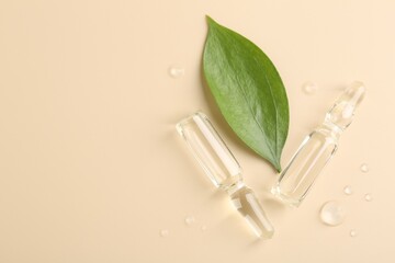 Glass ampoules with cosmetic product, leaf and water drops on beige background, flat lay. Space for text