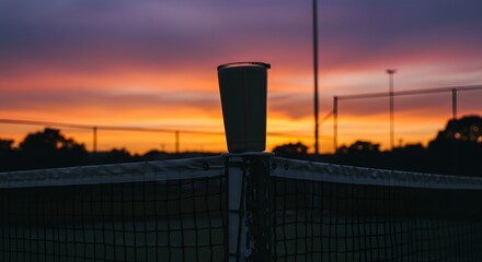 Tennis, Tennisschläger und Tennisball am Tennisplatz, tennis court. A solitary cup rests atop a tennis net against a vibrant, colorful sunset backdrop.