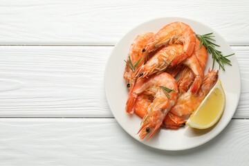 Delicious seafood dish. Tasty grilled shrimps served with rosemary and lemon on white wooden table, top view. Space for text