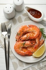 Tasty grilled shrimps served with rosemary, sauce and lemon on white wooden table, flat lay. Delicious seafood dish