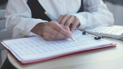 A businesswoman focuses on organizing paperwork and entering data into a computer. She is seated at a modern office desk, demonstrating professionalism and diligence during work hours