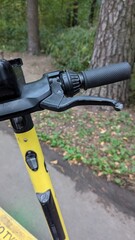 close-up of the handlebars of a yellow electric scooter, with the brake lever prominently visibl