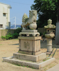 A stone statue of a shrine guardian dog (Komainu) and a stone lantern stand in the shrine garden.
Real dogs are resting behind them.
The stone monument's inscription reads '5 Yen.'