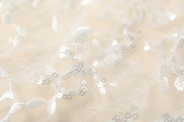 Fototapeta premium Beautiful lace fabric with sequins on beige background, closeup
