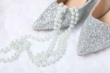 Beautiful shoes, pearl necklace and lace fabric on white background, closeup