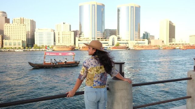 young woman at Dubai creek with traditional Abra boat sailing and old Dubai buildings background, 4k prores travel video  