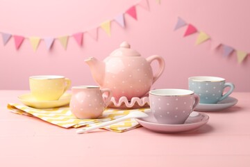 Beautiful ceramic tea set for children on wooden table against pink background with party flags, closeup