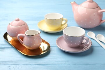 Beautiful ceramic tea set for children on light blue wooden table, closeup