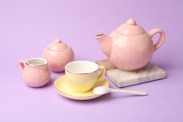 Beautiful ceramic tea set for children on violet background, closeup